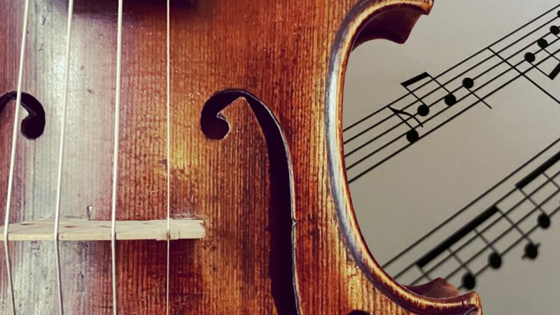 Symbolbild Adventskalender: Ausschnitt einer Geige im Vordergrund. Dahinter schauen Noten hervor.